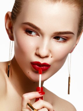 Makyaj ürünleri. Altın küpe ve yüzük beyaz arka plan üzerinde gülümseyen genç güzel kız. Kırmızı tırnak manikür işinde. Dudak parlatıcısı uygulayarak moda aksesuarları ile genç bir kadın