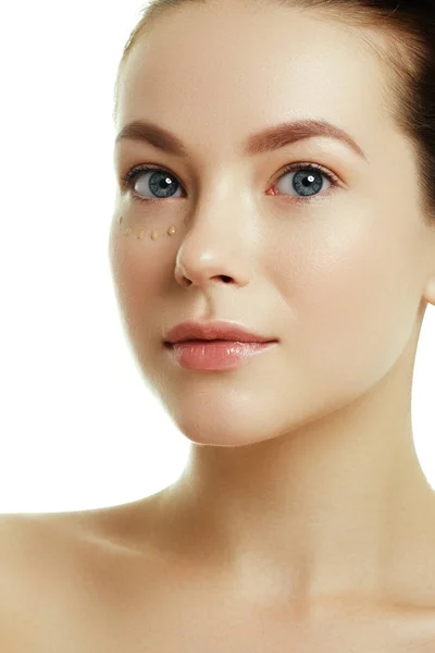 Maquillaje diario. Concepto de belleza. Mujer joven con gotas de crema en su hermoso rostro sobre fondo blanco. Saludable y spa. Belleza natural. Mujer aplicando crema cosmética en su cara bonita — Foto de Stock