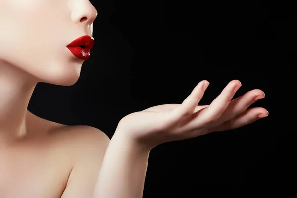 Красивая молодая женщина, выдыхающая поцелуй из своей руки. Модель с идеальным темно-красные губы и маникюрные красные ногти — стоковое фото