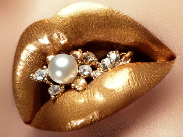 Cosméticos e maquilhagem. Fechar os lábios artísticos de ouro. Brilho maquiagem labial brilhante. Atirar de uma menina bonita com batom dourado e brilho. Lábios sexy e elegante. Pérolas e diamantes na boca — Fotografia de Stock