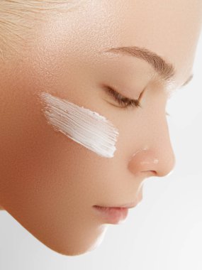 Yüzüne krem süren güzel bir kız. Gençlik ve cilt bakımı konsepti. Beyaz tenli, izole bir kadın yüzü portresi.