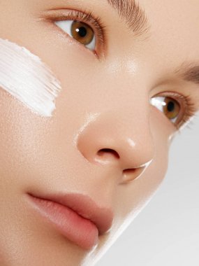 Yüzüne krem süren güzel bir kız. Gençlik ve cilt bakımı konsepti. Beyaz tenli, izole bir kadın yüzü portresi.