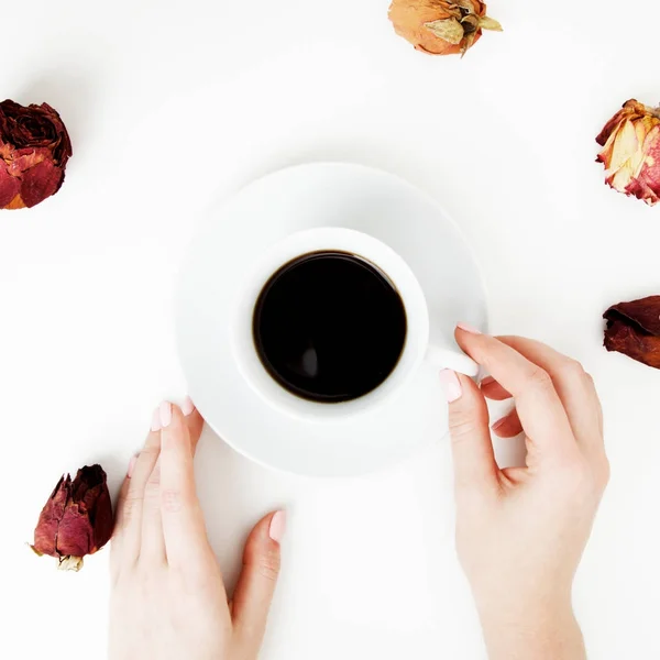 Acostado. Vista superior. Estilo mínimo. Moda minimalista y fotografía de belleza. De buen humor. Una niña con manicura sostiene una taza de café blanco sobre un fondo de mesa blanco. Pétalos de rosa alrededor de la copa — Foto de Stock