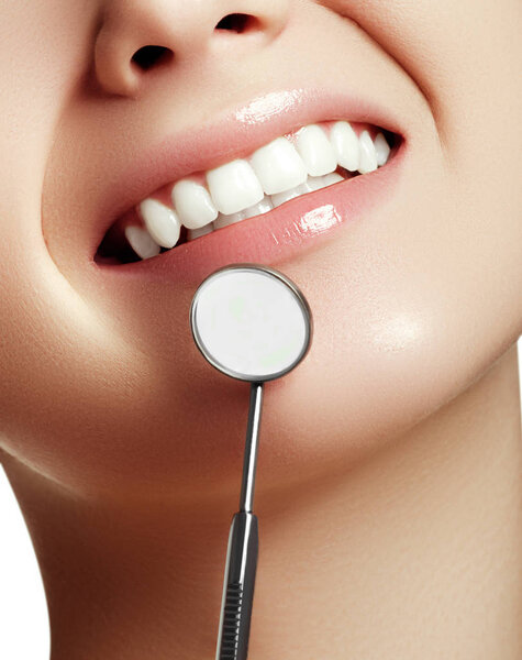 Женская улыбка. Зубы здоровой белой женщины и зеркало зубоврачебного рта крупным планом. Гигиена зубов, концепция полости рта. Обследование в стоматологии с помощью стоматологических инструментов. Отбеливание зубов. Концепция стоматологии
