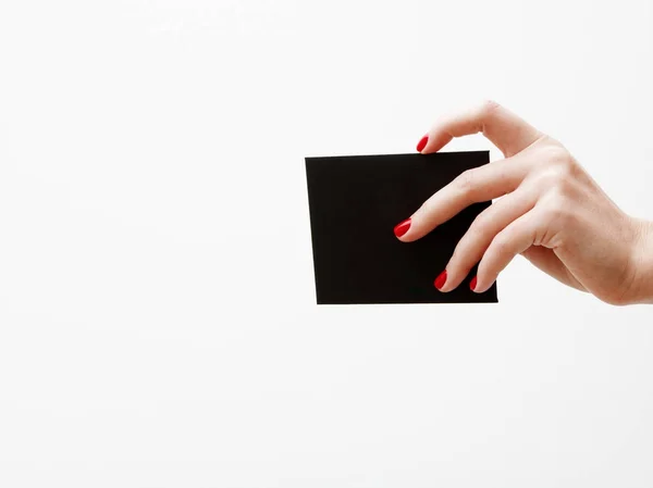 Deitado plano, vista superior. Conceito de beleza e moda. Belas mãos femininas com manicure vermelho. Estilo mínimo. Fotografia minimalista. Composição com a mão da menina segurando cartão de desconto no fundo branco — Fotografia de Stock