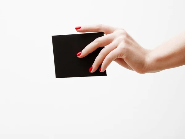 Deitado plano, vista superior. Conceito de beleza e moda. Belas mãos femininas com manicure vermelho. Estilo mínimo. Fotografia minimalista. Composição com a mão da menina segurando cartão de desconto no fundo branco — Fotografia de Stock