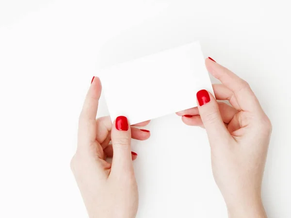 Flat lay, top view. Beauty and fashion concept. Beautiful female hands with red manicure. Minimal style. Minimalist photography. Pale composition with girl's hand holding card on white background — Stock Photo, Image