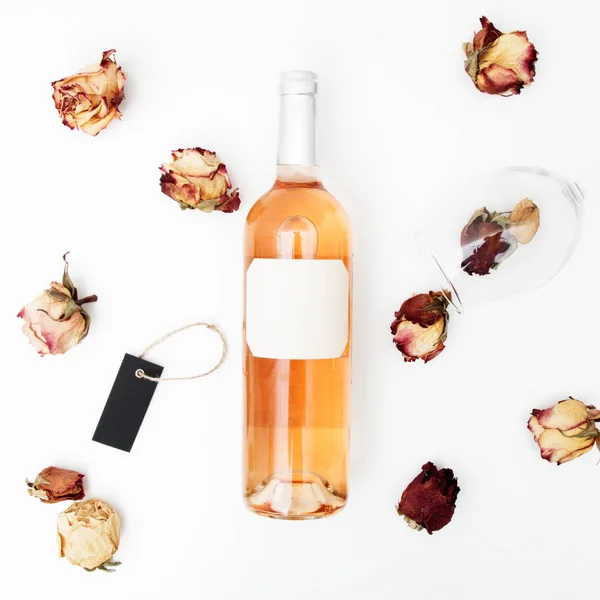 Flat lay. Minimal style. Minimalist trend photography. A bottle of rose with a composition of dried roses. Wine bottle, glass and on white table. Top view