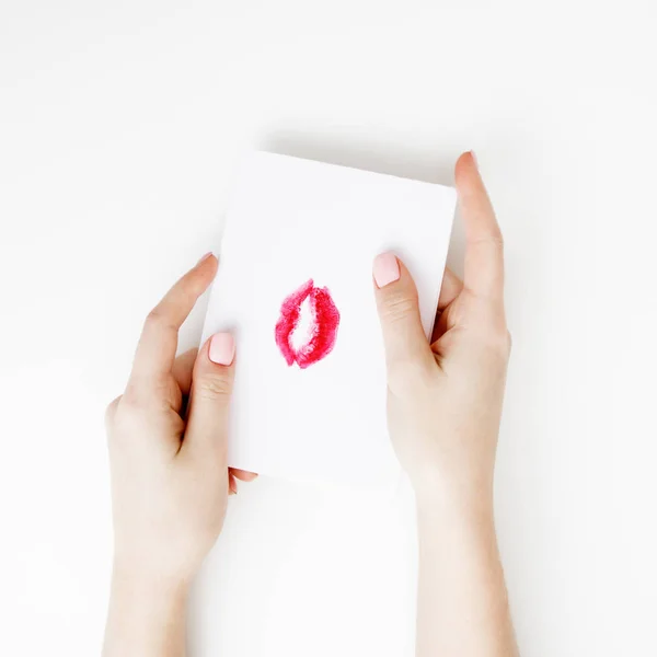 Flat lay. Top view. Hand of girl writing love letter on Saint Valentines Day. Handmade postcard with red lips shaped figure. Woman draw kiss on postcard for 14 February holiday celebration