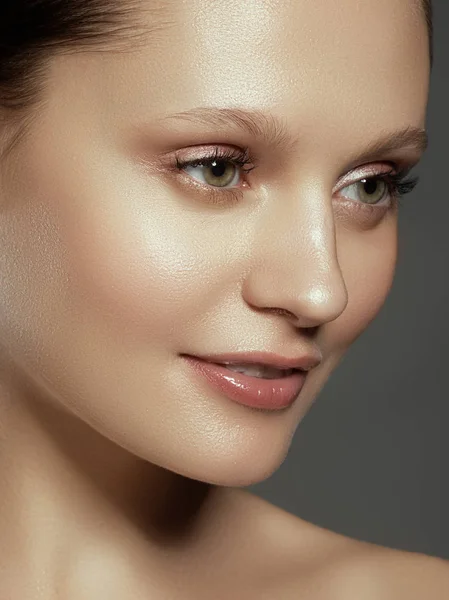 Gözleri iri ve kara kaşları, bir model ile hafif çıplak makyaj, gri studio arka plan, güzellik Foto, gülümseyen güzel kızla yakın çekim. Güzel spa modeli kız mükemmel taze temiz deri ile