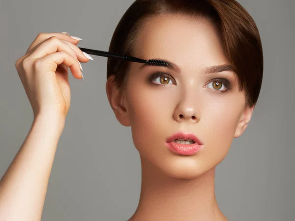 Güzel genç kadın yüzünü fırça gri arka plan üzerinde izole bir makyaj ile vakıf uygulayarak — Stok fotoğraf