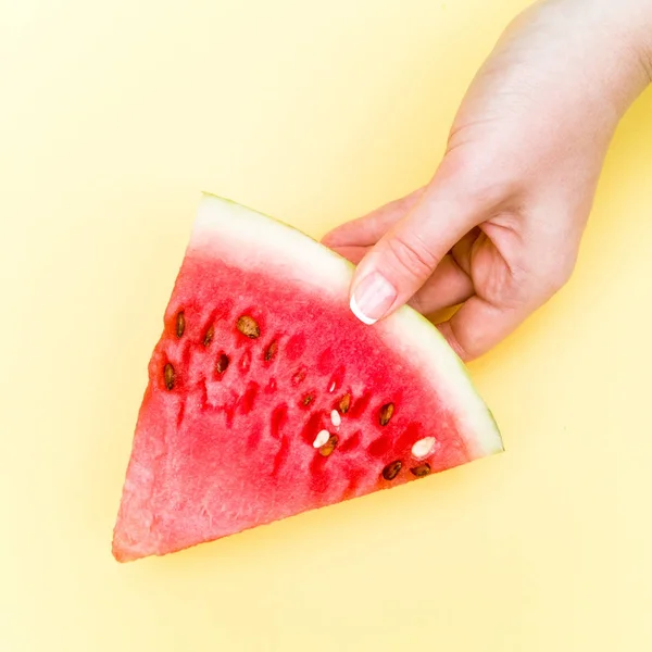 Flat lay. Top view. Young woman is holding slice of watermelon over colorful yellow background. Nail art manicure. Nail Polish. Beauty hands
