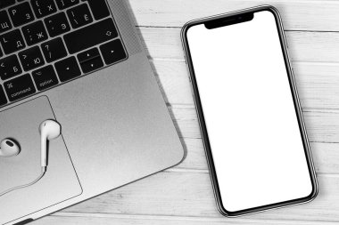 Kulaklıklı iPhone modeli ve Apple Macbook beyaz ofis masasına yakın çekim yapıyor. Grafik görüntüleme için boş ekran cep telefonu. Moskova, Rusya - 23 Aralık 2019