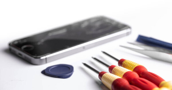 broken smartphone Apple iPhone SE preparing to repair or replace new part, screwdrivers and tweezerson white background. Moscow, Russia - December 26, 2019