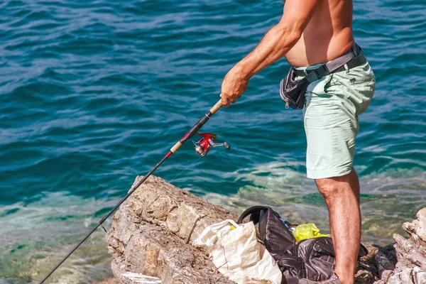 Мужчина ловит рыбу, стоя на берегу, солнечный день рыбалки на — стоковое фото