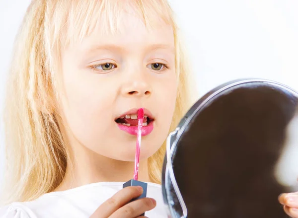 Little happy girl paints lips looking in the mirror