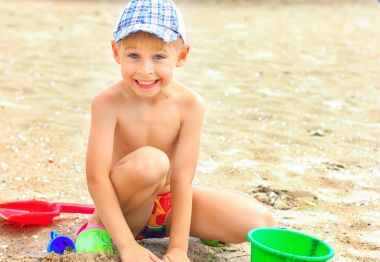 Küçük çocuk kumsalda kumla oynuyor.