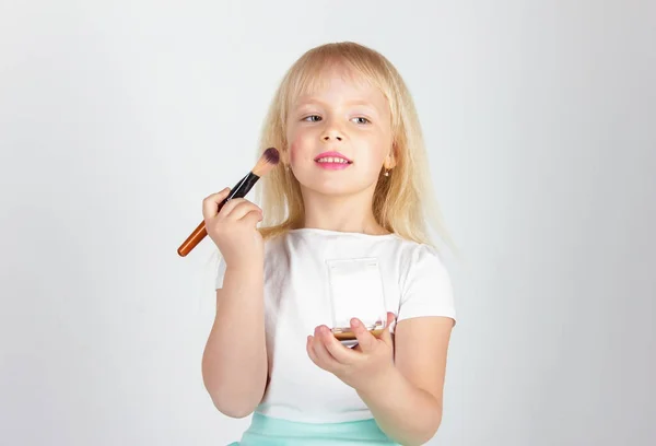 Happy little girl paints face make-up with mirror in on white in — Stock Photo, Image