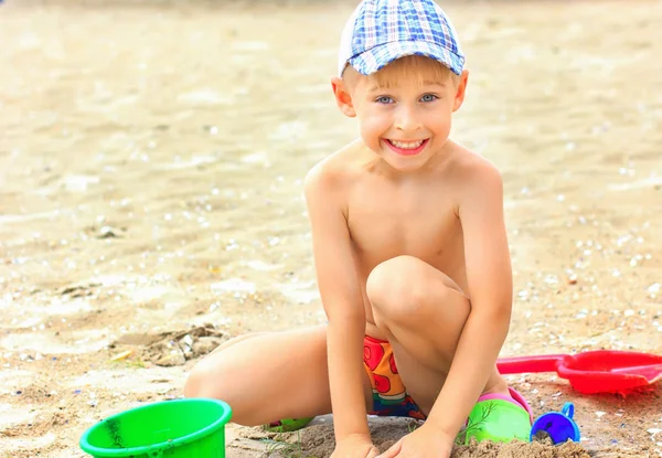 Küçük çocuk kumsalda kumla oynuyor.