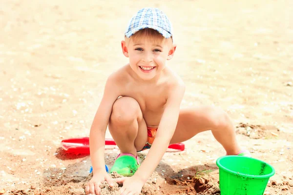 O rapazinho está a brincar com areia na praia. Verão, edifício c — Fotografia de Stock