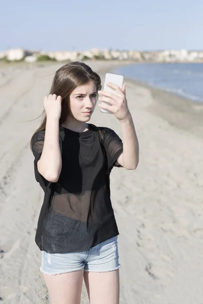 Mujer joven en una playa mirando su móvil . — Foto de Stock