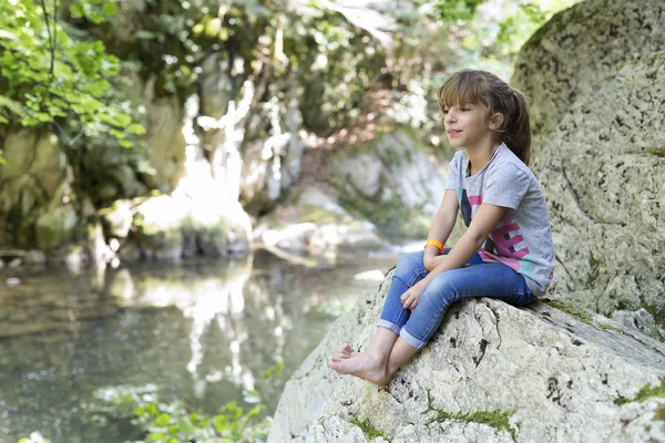 Bir kaya şelale yanında oturan kız.