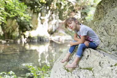 Girl sitting on a rock next to the Waterfall. clipart