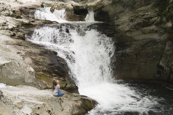 Chica sentada en una roca junto a la cascada . —  Fotos de Stock