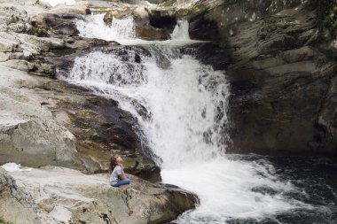 Bir kaya şelale yanında oturan kız.