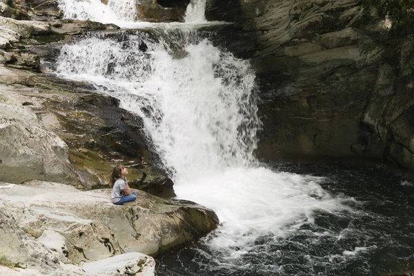 Bir kaya şelale yanında oturan kız.