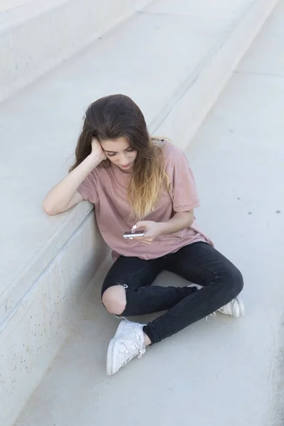 Adolescente sentada en una escalera con su móvil buscando . — Foto de Stock
