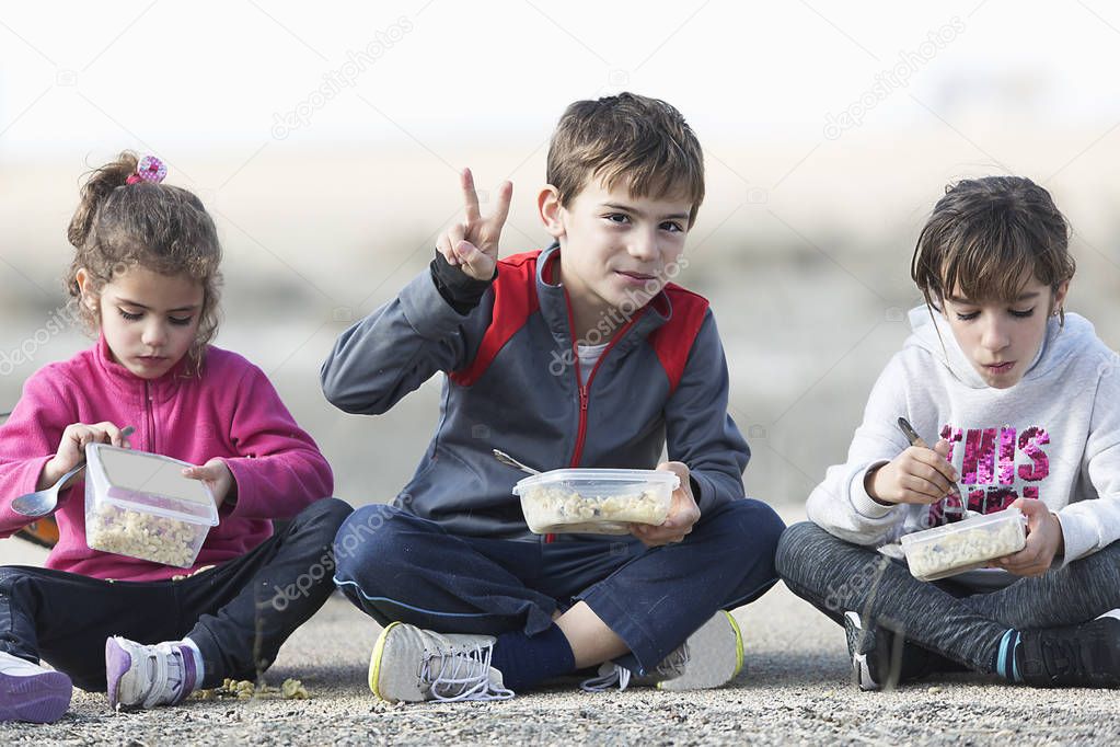 Three children sitting on floor taking outdoor snack.