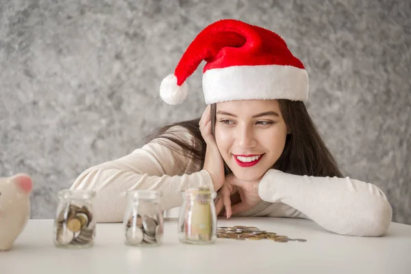 Young woman with red christmas hat looing at piggy bank — Stock Photo, Image