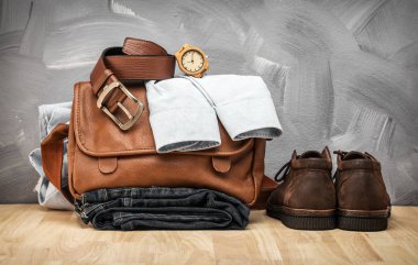 Asya vintage tarzı erkek giyim ve kot pantolon ve çanta ahşap masanın üstüne koy ve beton duvar doku arka plan çatı.