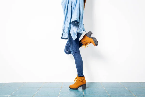 Mladá dívka modré džíny a hnědé boty stěna bílá. — Stock fotografie