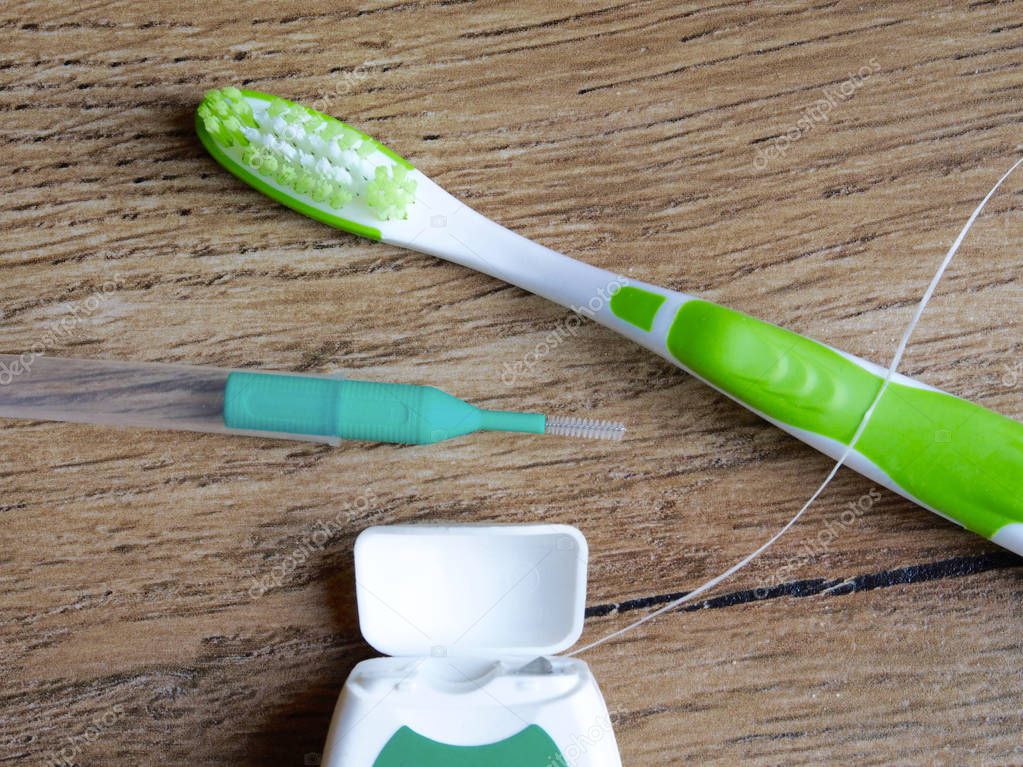 Dental floss, interdental brush and toothbrush on wood background