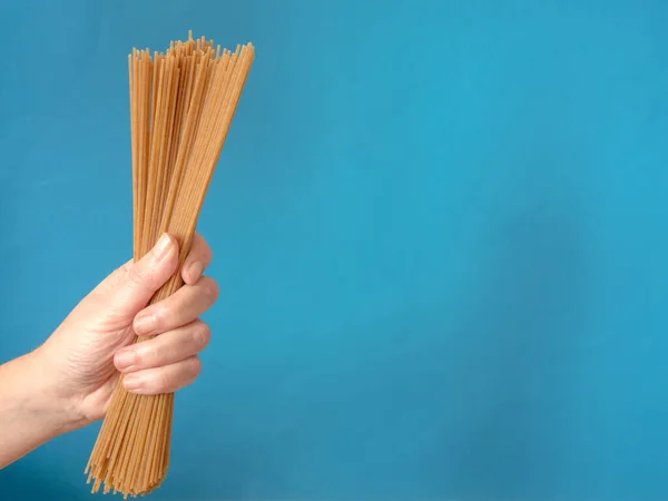 Hand Met Volkoren Rauwe Spaghetti Blauwe Achtergrond Met Kopieerruimte — Stockfoto