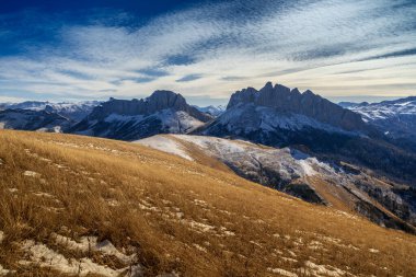 Ön planda sarı, dağın yamacında sonbahar otları, arka planda bulutlu mavi bir gökyüzünün altında güzel kayalardan oluşan bir duvar var..
