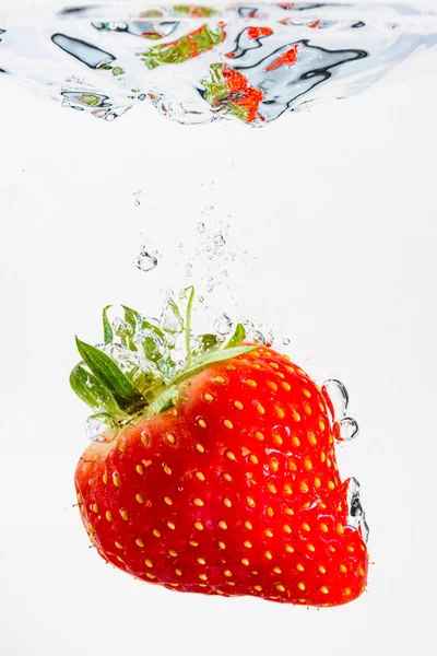 Fresa cae profundamente bajo el agua con un gran chapoteo. Fruta que se hunde en agua clara sobre fondo blanco — Foto de Stock