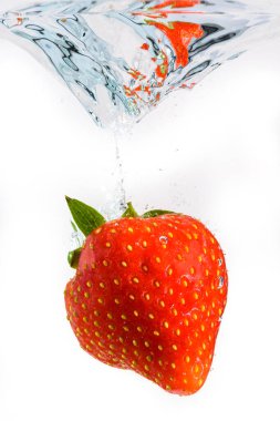 Çilek büyük bir su sıçramasıyla derin bir şekilde suya düşer. Meyveler beyaz zemin üzerinde berrak suya batar