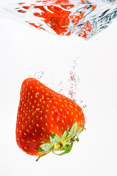 Fresa cae profundamente bajo el agua con un gran chapoteo. Fruta que se hunde en agua clara sobre fondo blanco — Foto de Stock