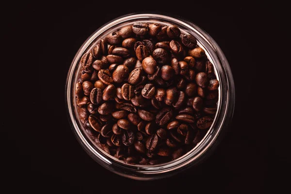 Grains de café en pot de verre debout sur fond noir . — Photo