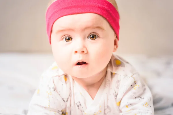 Entzückende 6 Monate alte Säugling auf einem Bett auf dem Bauch mit dem Kopf nach oben in die Kamera blickend mit ihren großen Augen. natürliches Licht. — Stockfoto