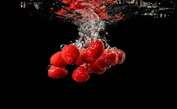 Rote Himbeeren fallen mit einem Spritzer unter Wasser, isoliert auf schwarzem Hintergrund. — Stockfoto