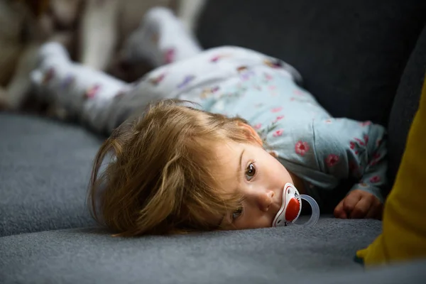 Niedliche 2-jährige Mädchen auf einem Bett auf dem Bauch mit dem Kopf auf dem Sofa. helles Interieur. — Stockfoto