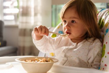 Two years old eats brakefast by herself with a spoon. Child development concept