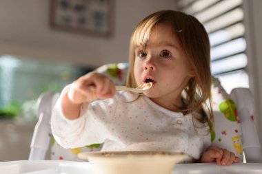 Two years old eats brakefast by herself with a spoon. Child development concept