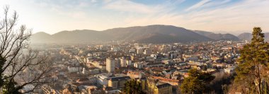 Graz, Styria Austria - 20.01.2019: Wide panorama of Graz City, City rooftops, residential area, mountains in background Sun in winter, blue sky. Travel destination.