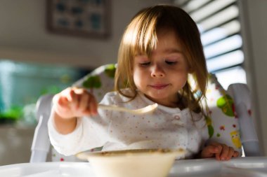 Two years old eats brakefast by herself with a spoon. Child development concept