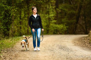 Genç bir kadın ormanda tasmalı bir av köpeğiyle yürüyor. Doğadaki boşluğu kopyala